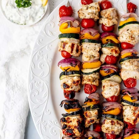 Four Greek chicken skewers on a white plate.