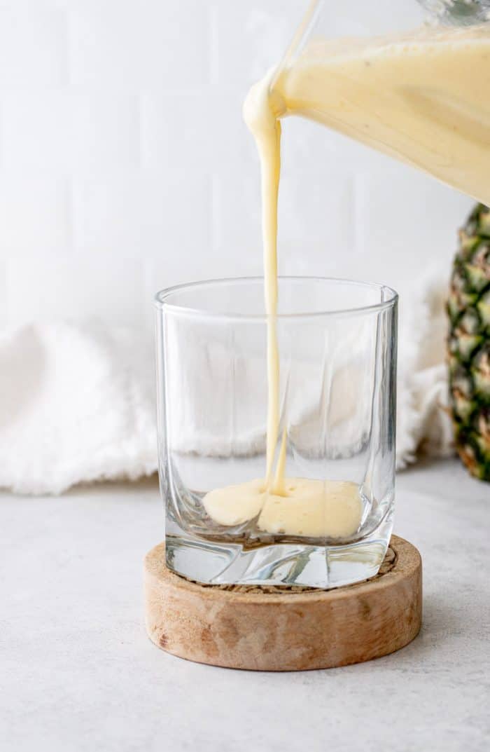 The pina colada smoothie being poured into a glass.