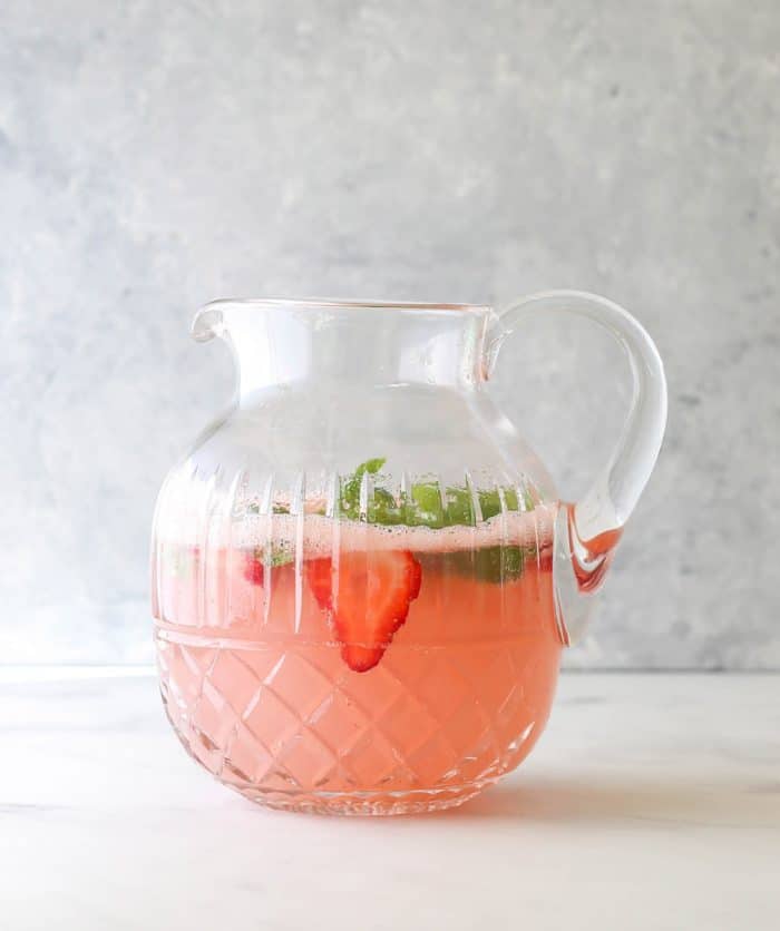 A strawberry mocktail spritzer in a jug garbished with basil and fresh strawberries.