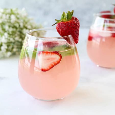 The strawberry mocktail in a glass garnished with fresh srawberries and basil leaves.