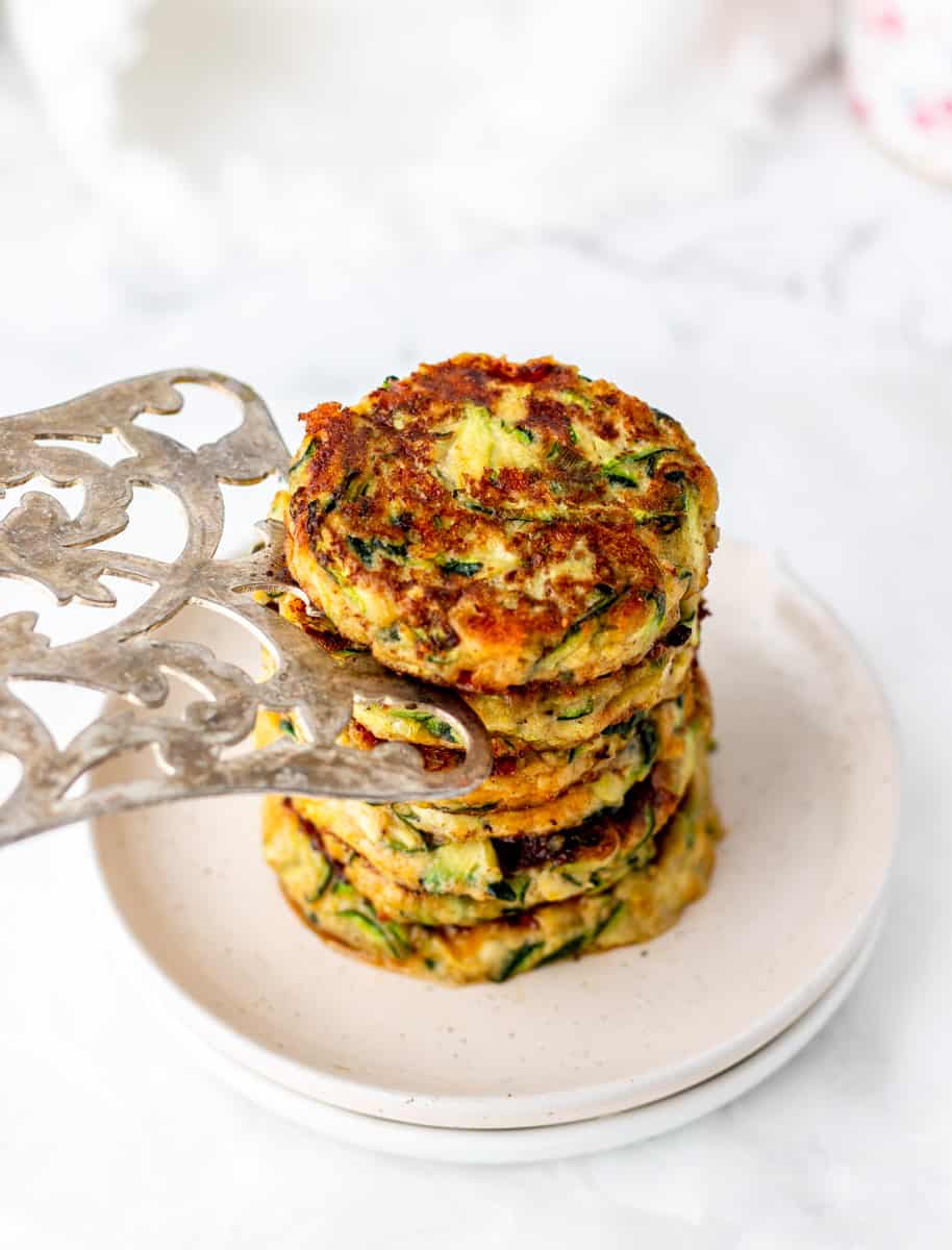 Stacking the zucchini fritters on to a plate with a metal spatula.