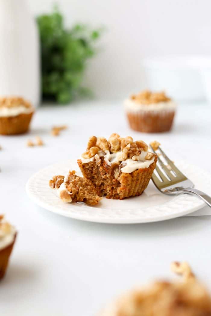A frosted carrot cake muffin on a plate with a fork.