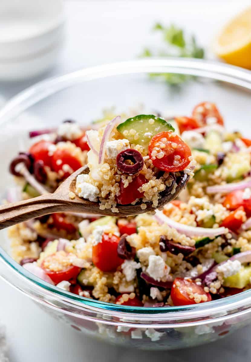 A spoon in a glass bowl of the Greek quinoa salad.