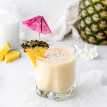 A pina colada smoothie in a glass next to a fresh pineapple.