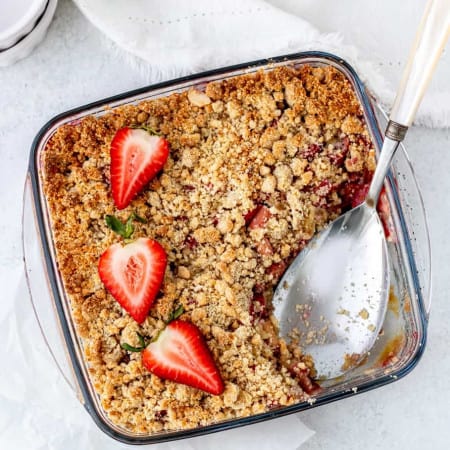 Strawberry rhubarb crumble in a glass dish with a serving spoon,