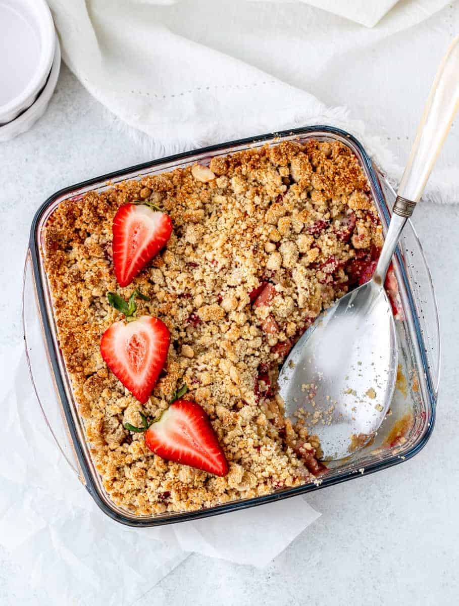 Strawberry rhubarb crumble in a glass dish with a serving spoon,