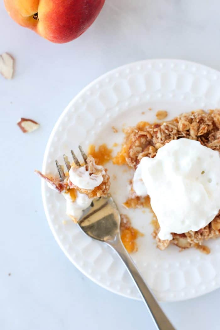 Overhead shot of a square of peach crumble on a plate with a fork.