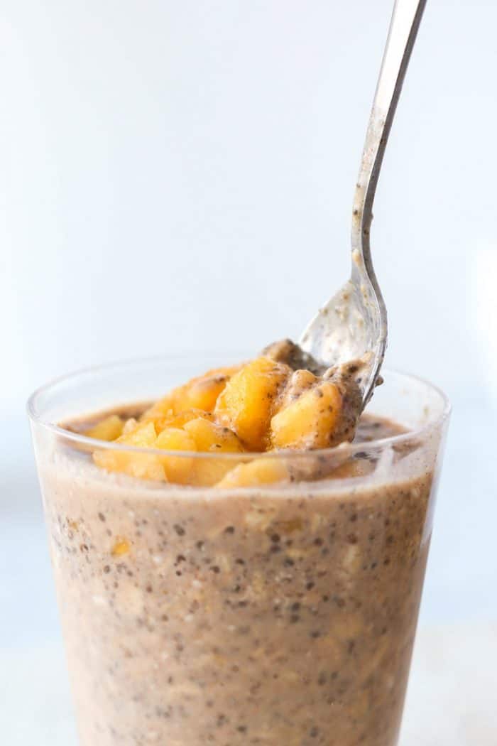 A spoon in a glass of peach overnight oats.