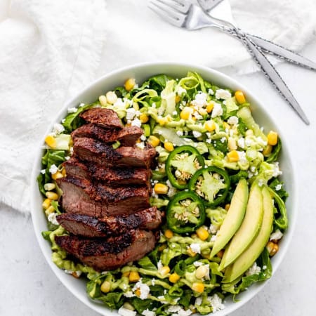 Overhead shot of steak salad with avocado green goddess dressing in a white bowl.