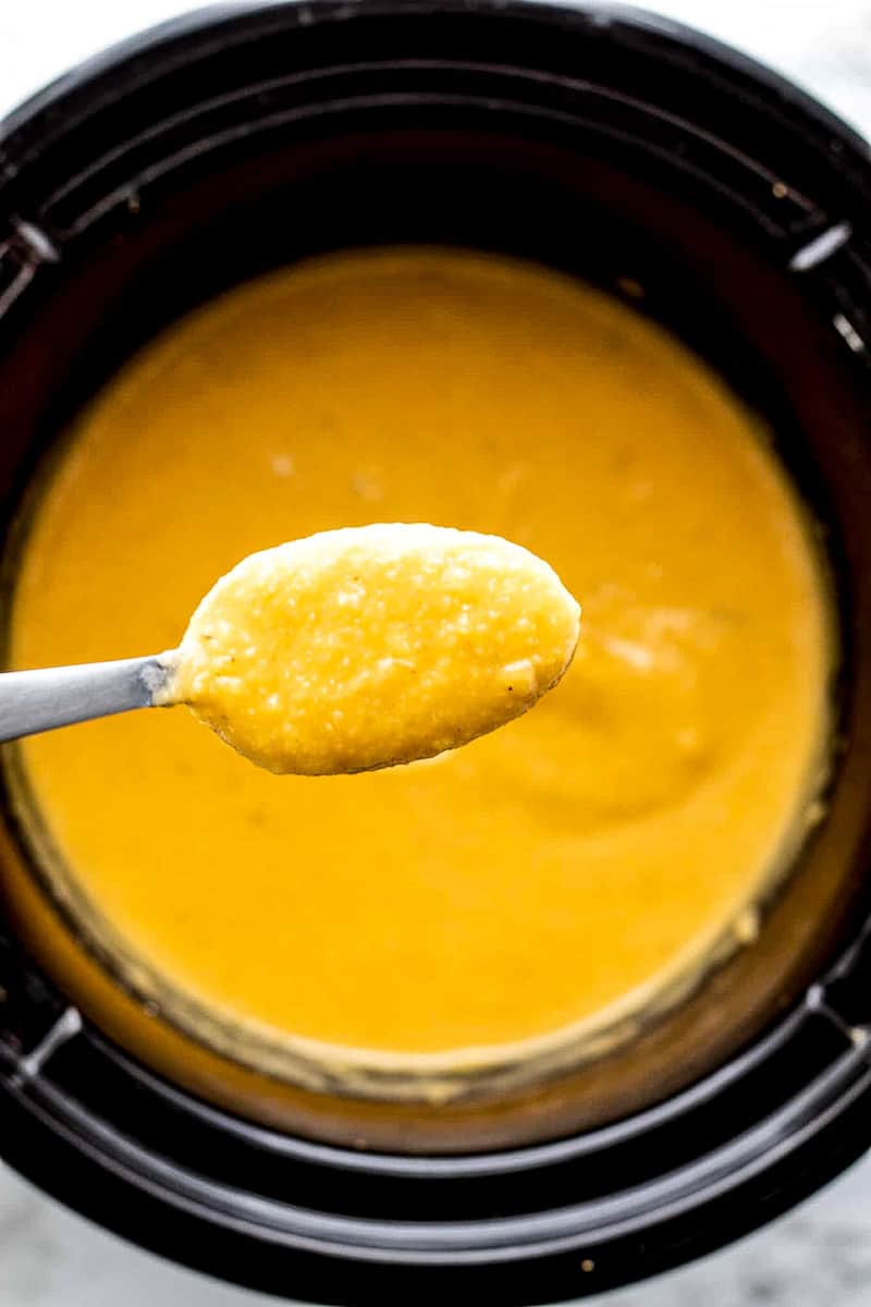 Butternut squash cheese sauce on a spoon over a crockpot.