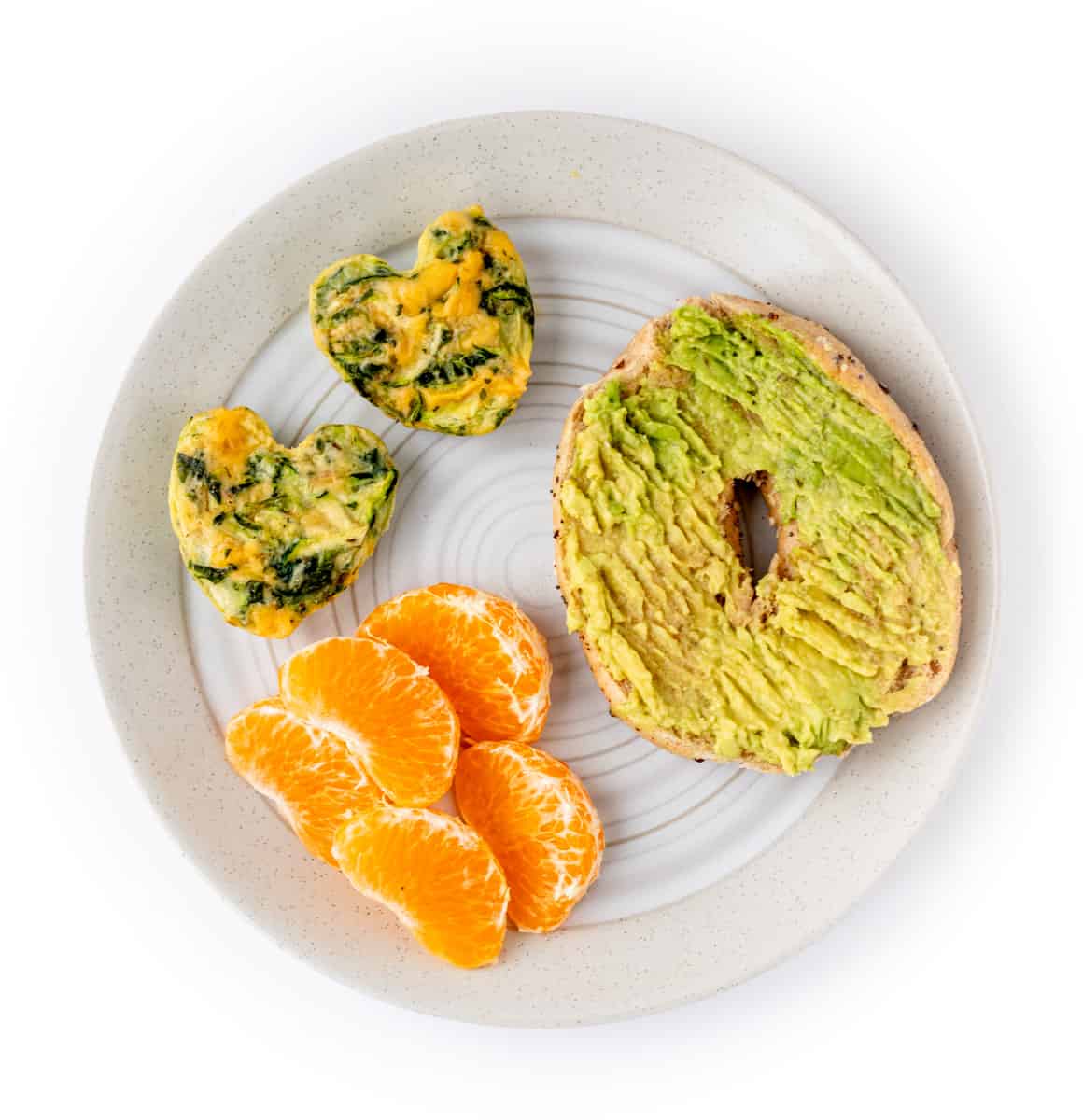 Frittata hearts with avocado mashed on a bagel with tangerine slices on a plate