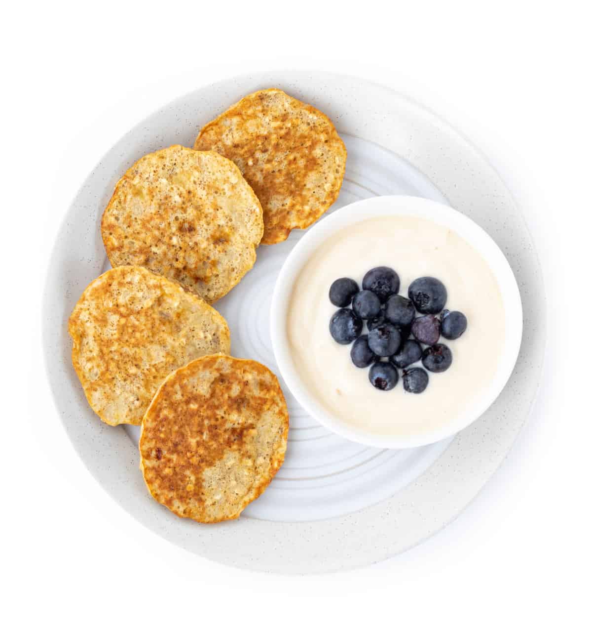Banana pancakes on a plate with a bowl of yogurt topped with blueberries