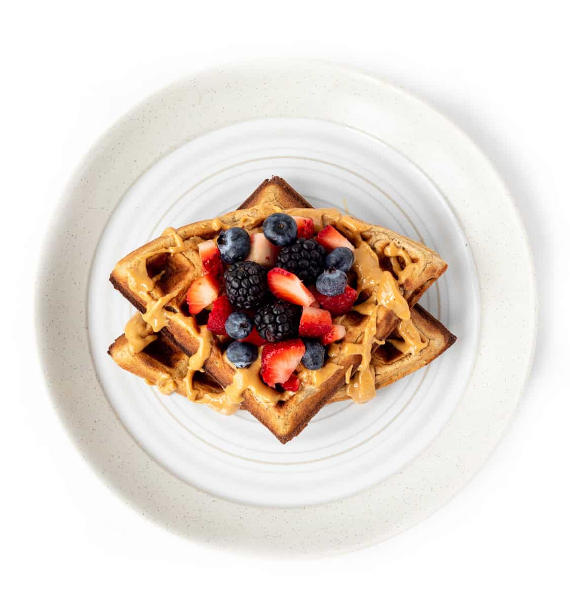 Two waffles on a plate with mixed berries and a drizzle of peanut butter on a plate