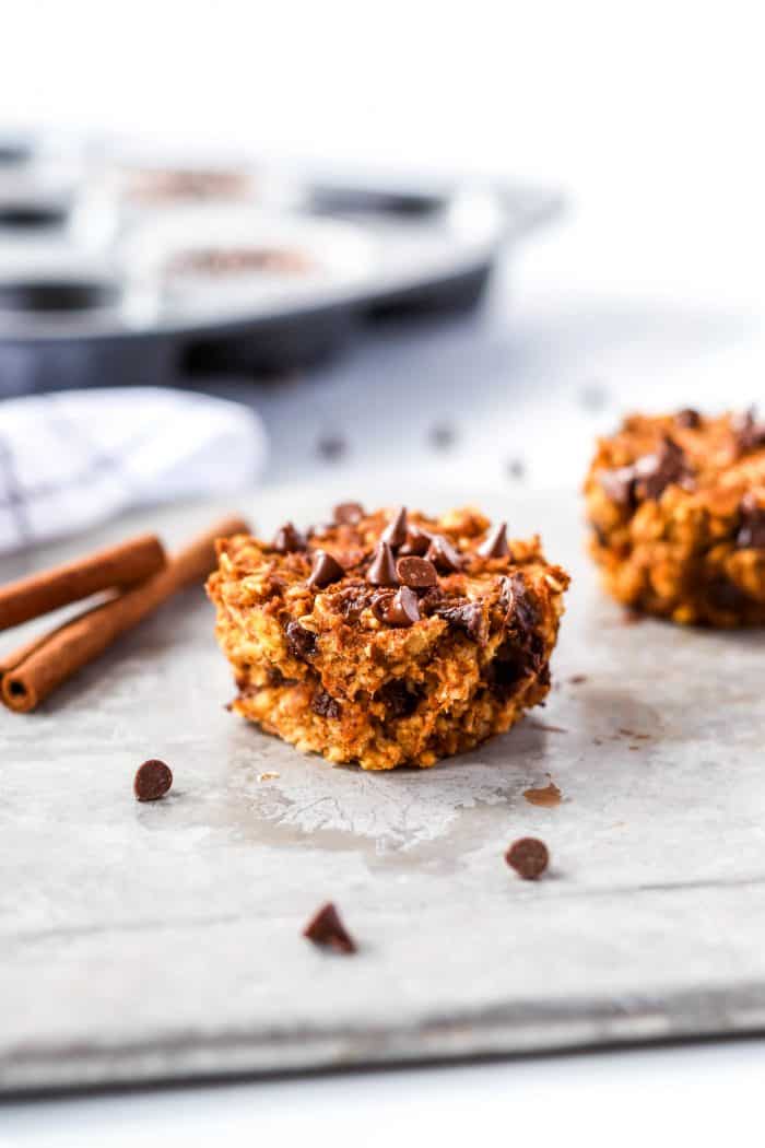 A pumpkin oatmeal muffin next to cinnamon sticks and chocolate chips.