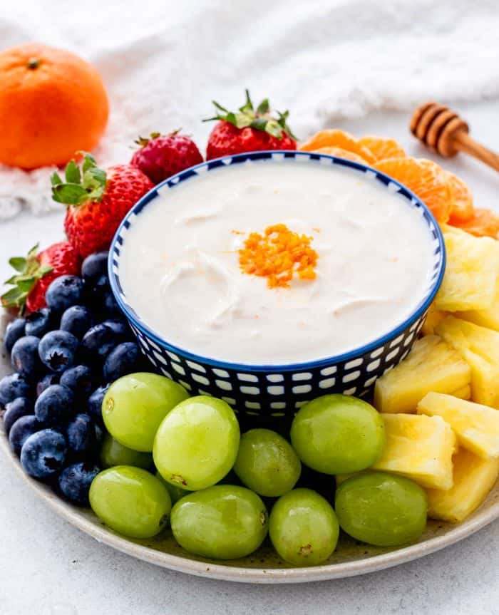A plate of fresh fruit with a bowl of yogurt dip in the middle.