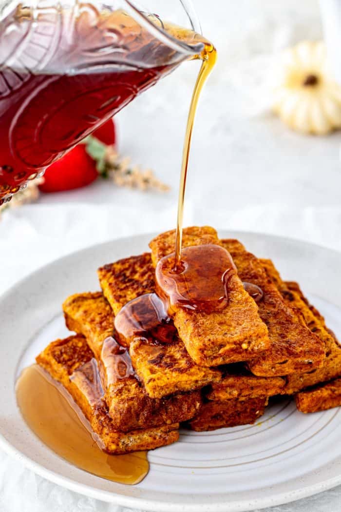 Maple syrup being poured over a stack of pumpkin French toast sticks.