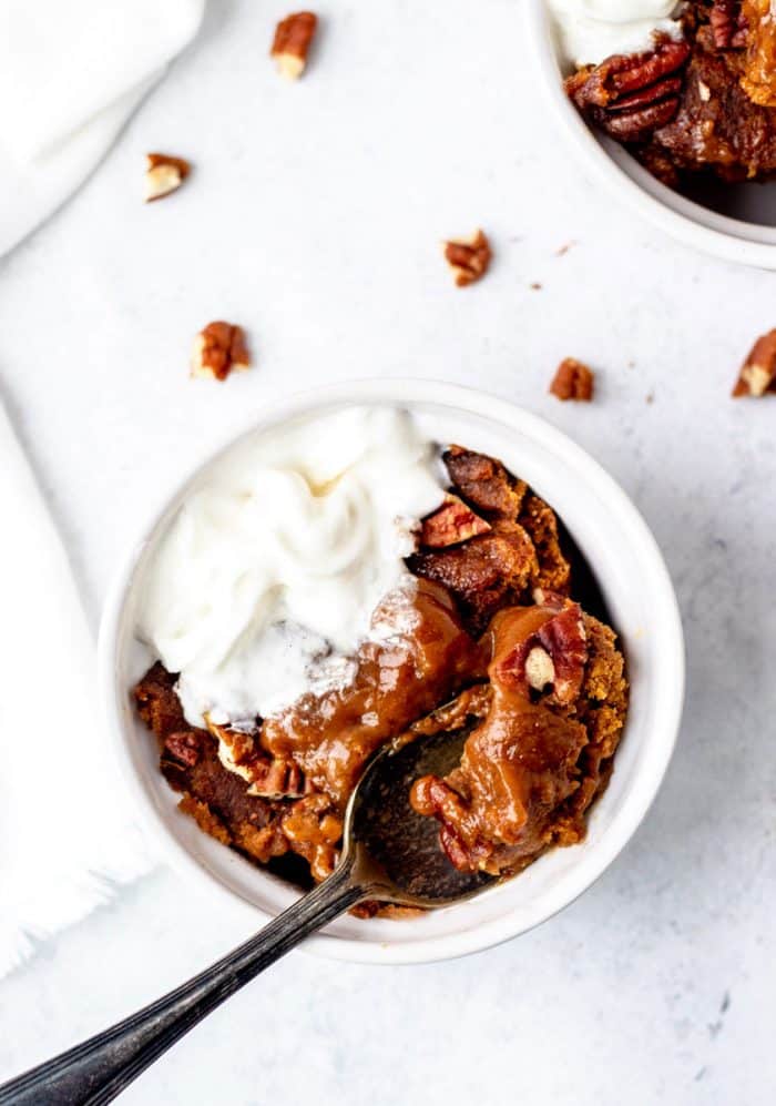 A spoon with pumpkin pudding cake and whipped cream in ramekin