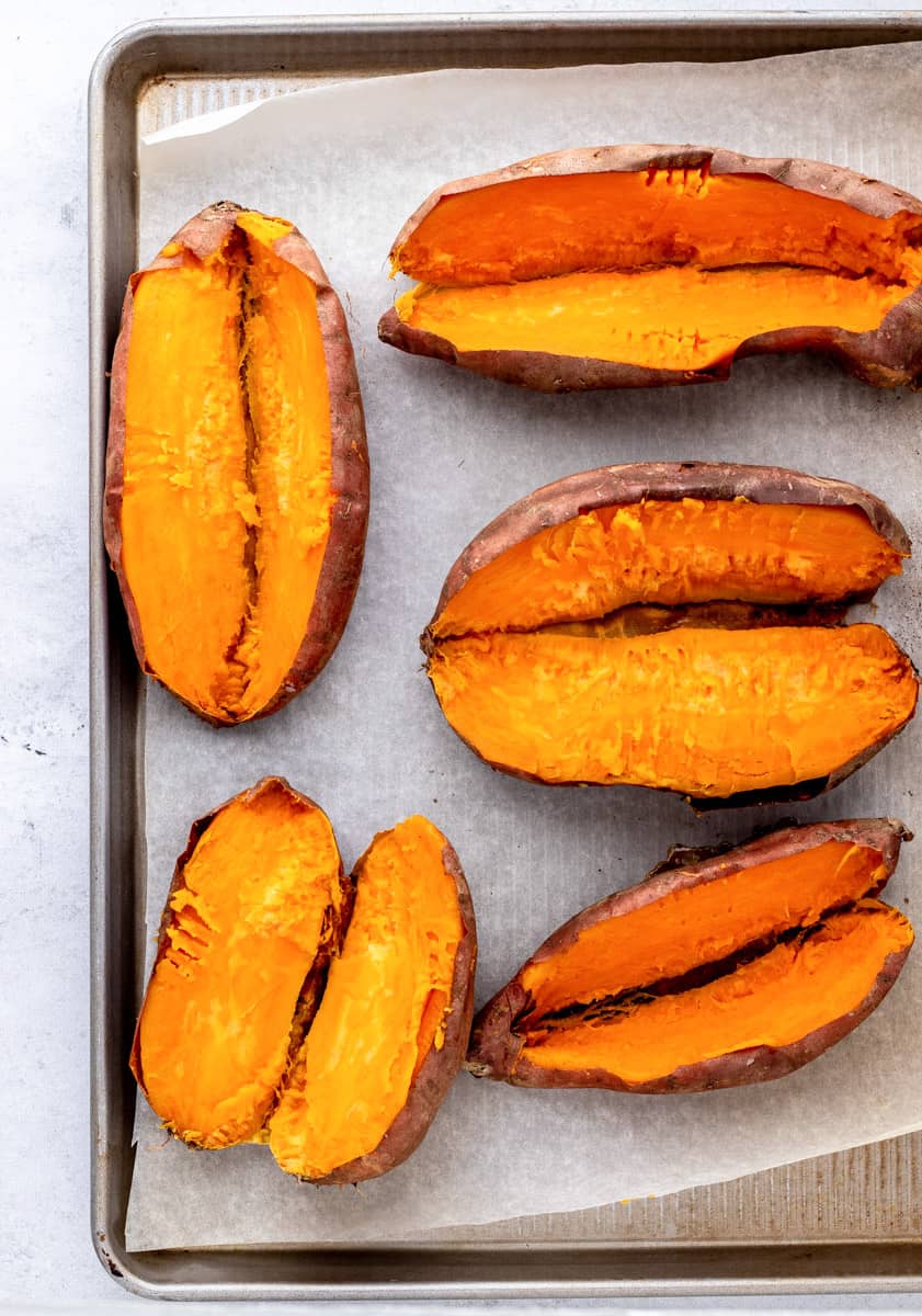 Baked sweet potatoes cut in half on a baking sheet