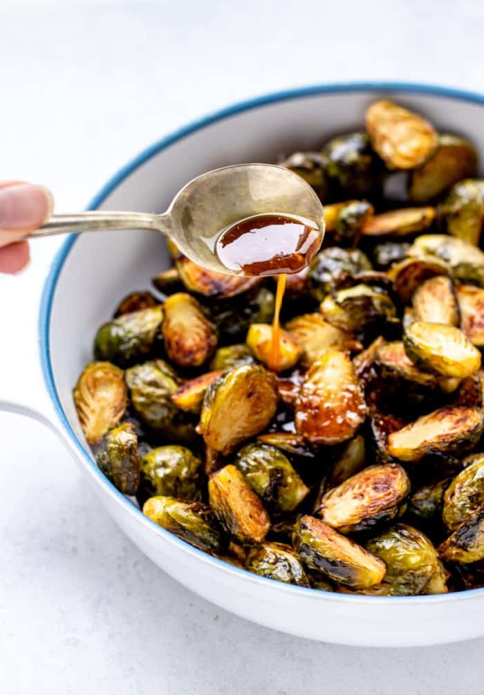 maple balsamic glaze on a spoon being drizzled on the brussel sprouts