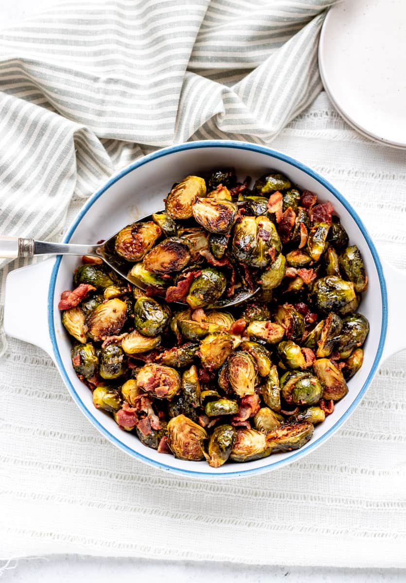 spoon scooping up brussel sprouts in a white and blue bowl next to serving plates