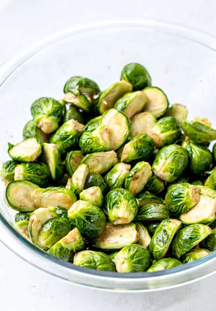 Halved brussel sprouts in a glass bowl with maple balsamic glaze