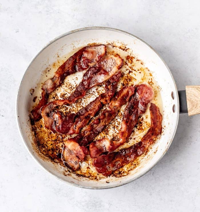 Bacon cooking in a white frying pan