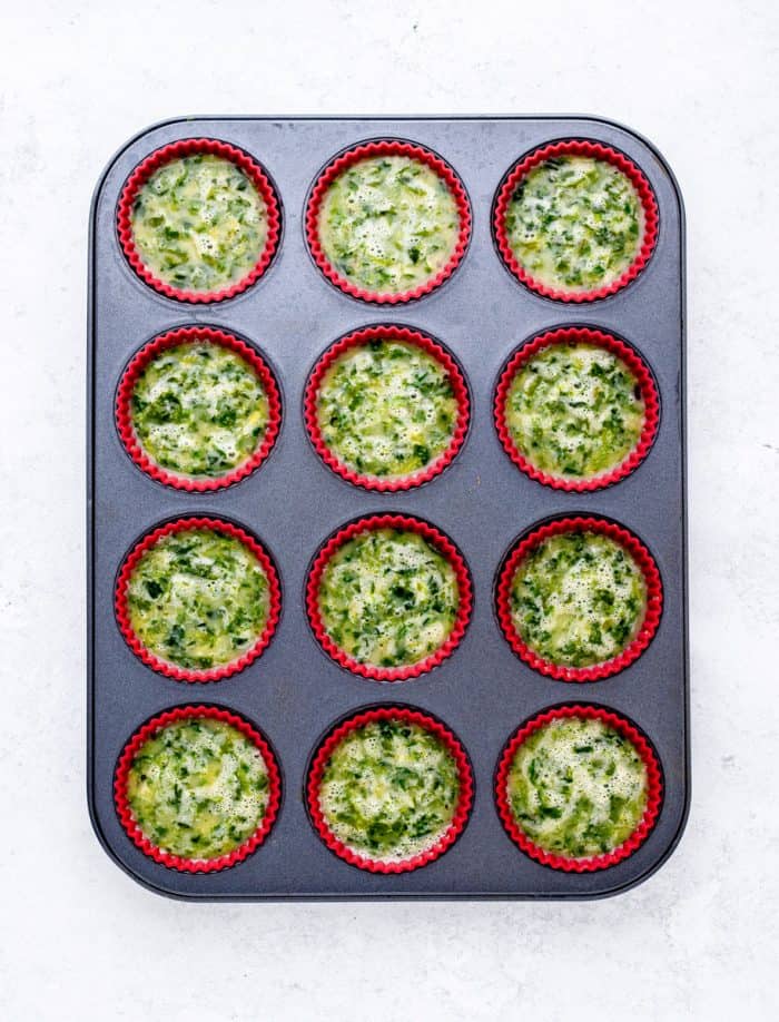 uncooked egg and spinach mixture in silicone cups in muffin tin