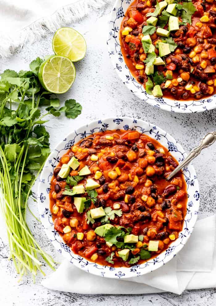 two blue and white bowls with bean chili topped with avocado and cilantro