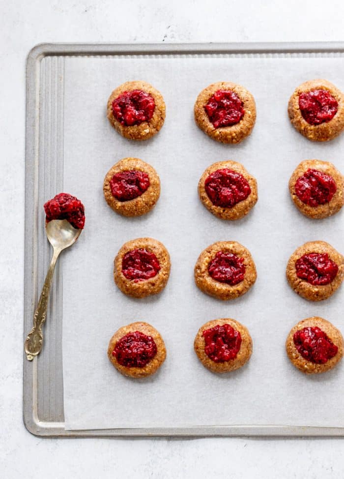 unbaked thumbprint cookies on baking sheet filled with jam next to a spoon