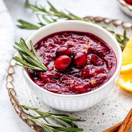 Healthy cranberry sauce topped with fresh cranberries in a bowl with sprig of rosemary.