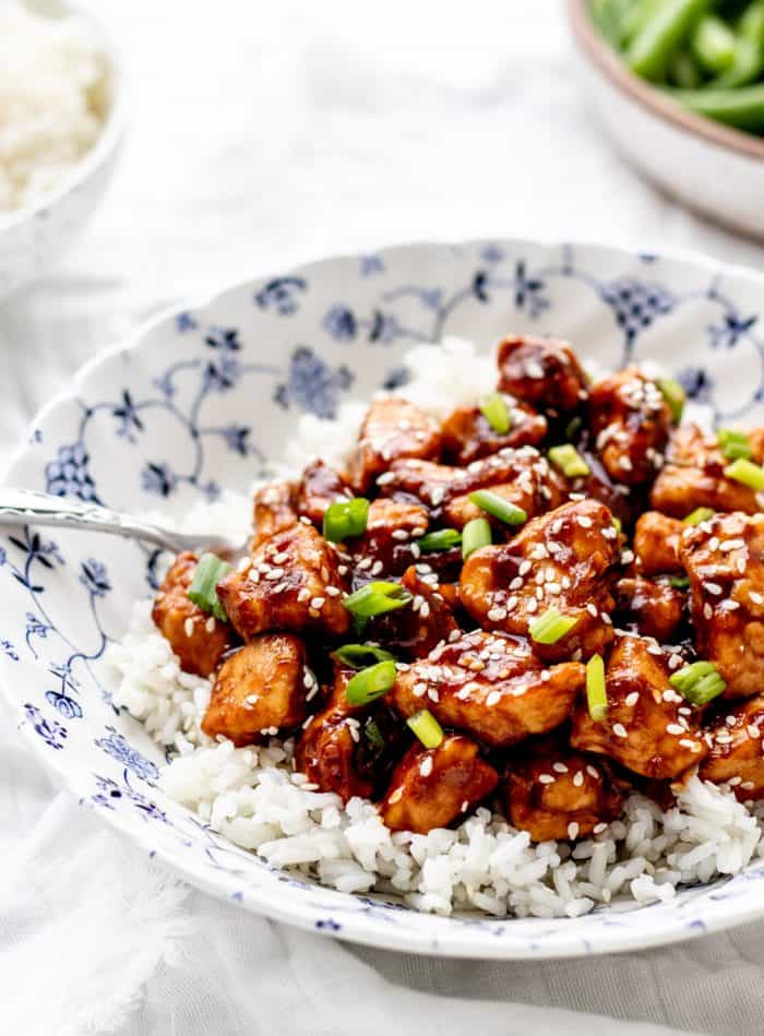 orange chicken in bowl on rice with sesame seeds and green onion