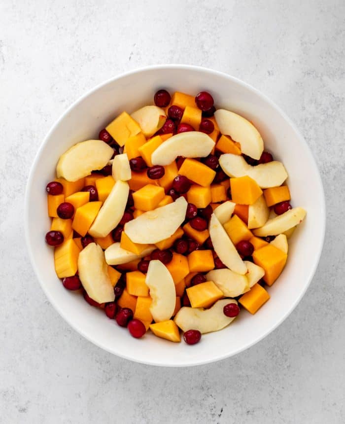 The butternut squash, apples and cranberries in a large white bowl