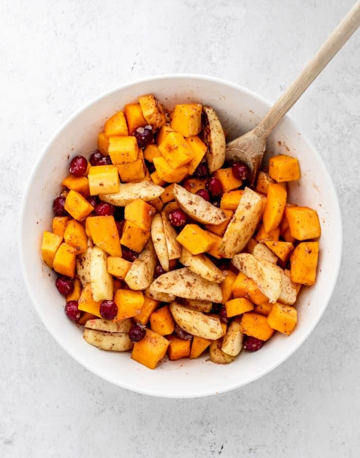 The squash, apples and cranberries tossed with spices in a large bowl with a wooden spoon