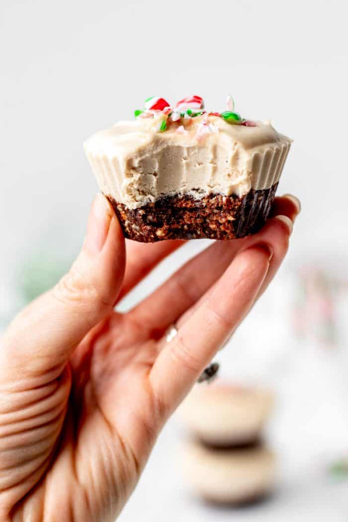 A hand holding up a cheesecake cup topped with crushed candycane with bite taken out of it