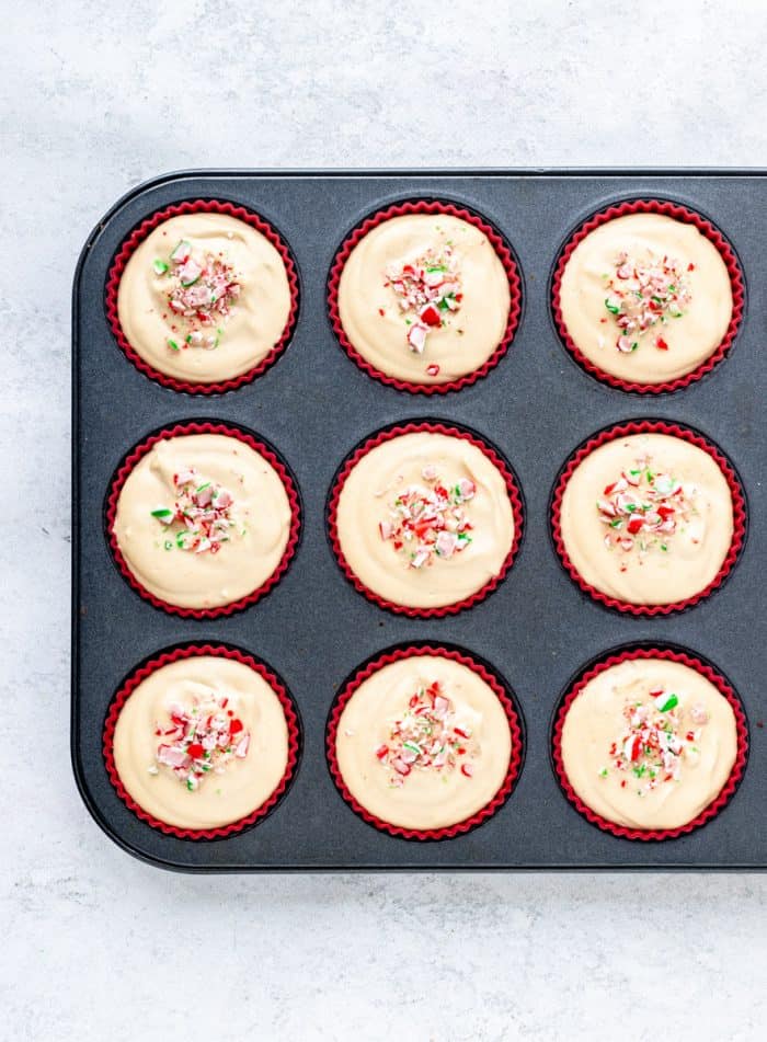 cheesecake bites in a muffin tin topped with candy cane ready to be frozen