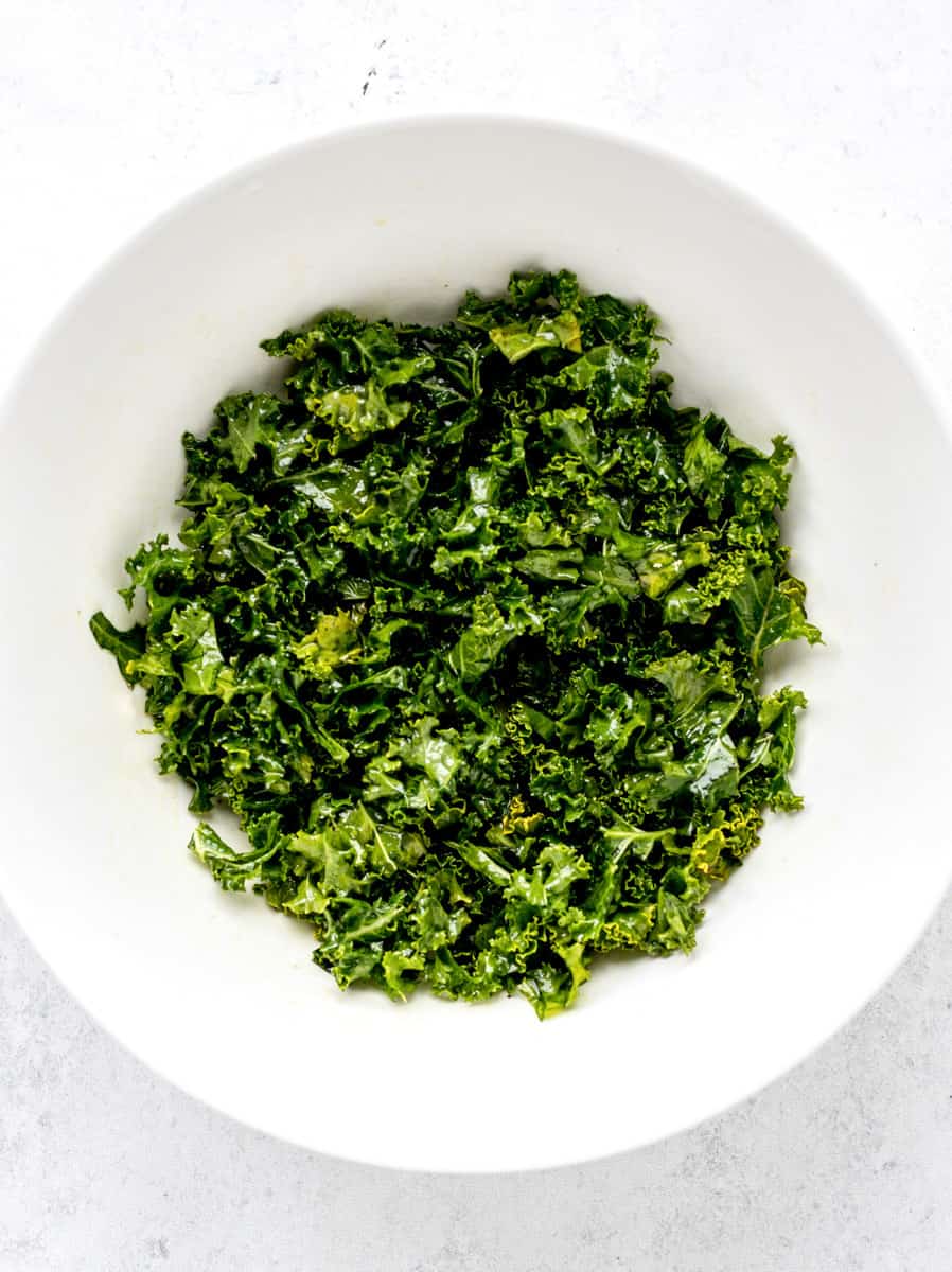 kale massaged with dressing in a big white bowl