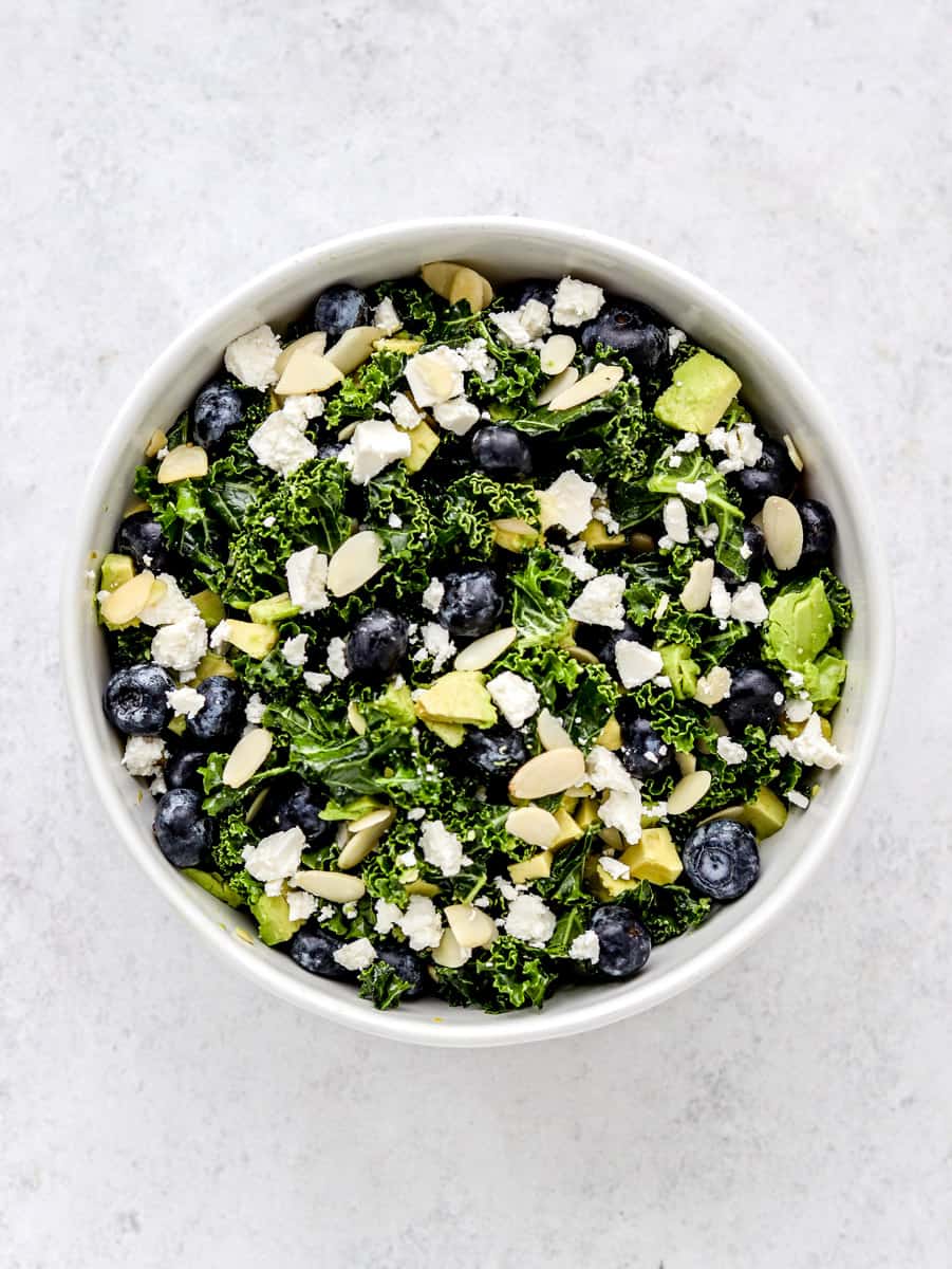 A bowl of avocado kale salad with blueberries and feta.