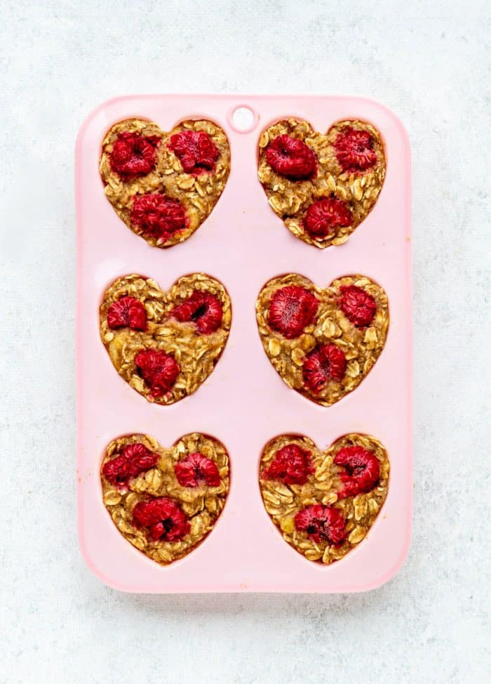 Baked oatmeal muffins with raspberries in a pink heart-shaped muffin mold.