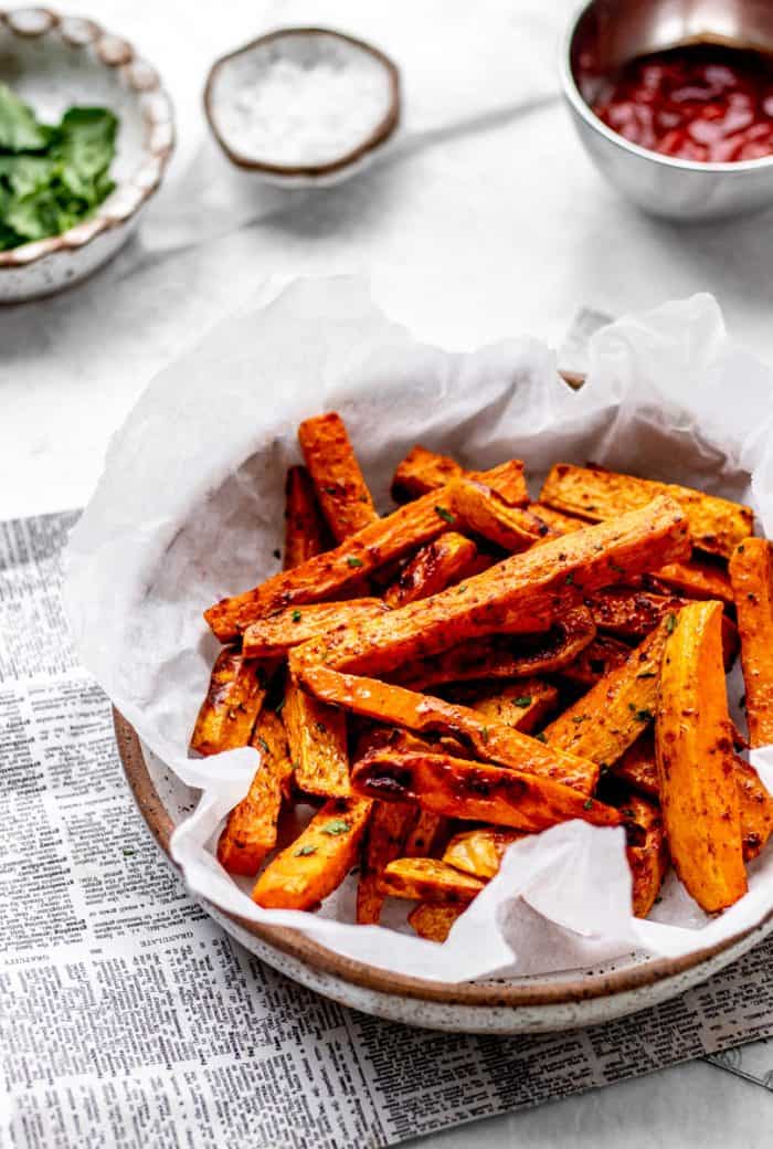 crispy sweet potato fries seasoned with cinnamon and paprika in a serving bowl lined with parchment paper.