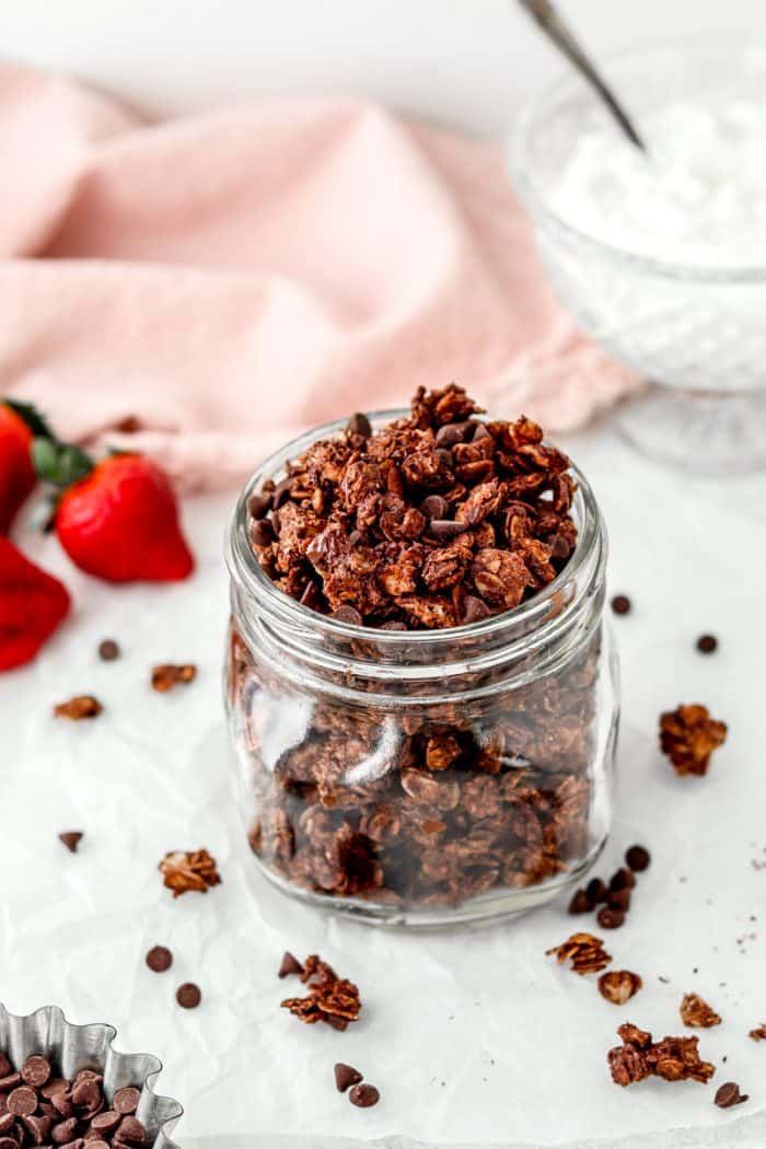 A jar of healthy chocolate granola next to fresh strawberries.