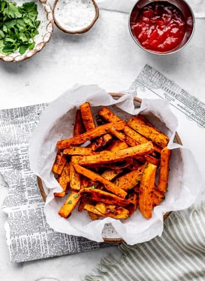 overhead shot of some oven baked sweet potato fries in a bowl lined with parchment paper.