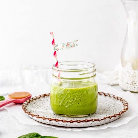 veggie green smoothie in a jar with a straw on a plate.