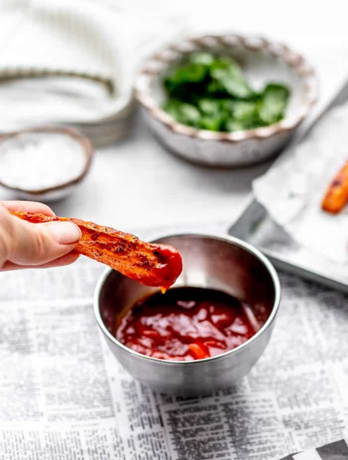 Dipping a sweet potato fry in a silver bowl of ketchup.