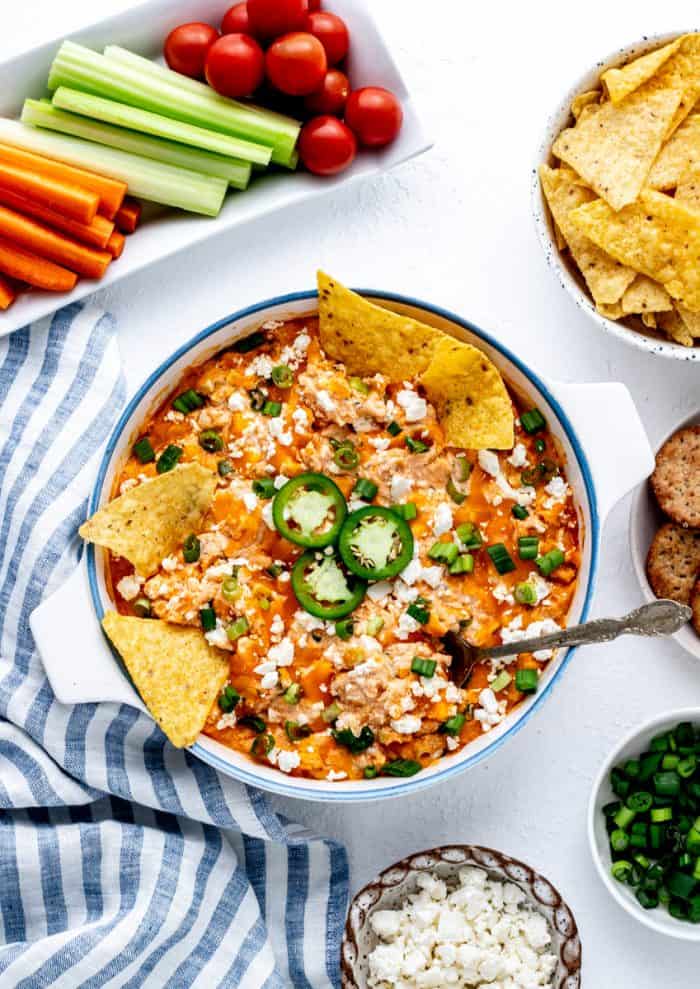 Healthier buffalo chicken dip in a serving dish with tortilla chips and a spoon dipped in.