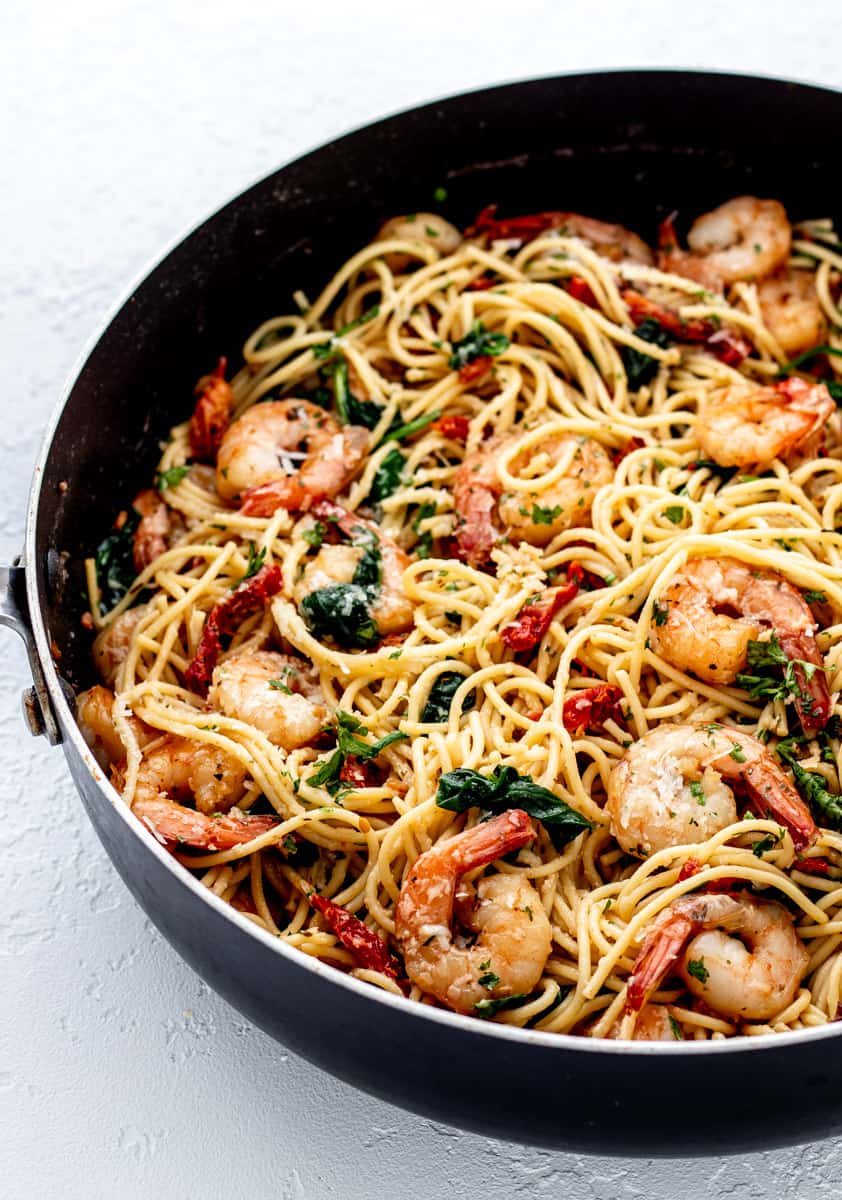 Close up of shrimp spaghetti in a pan with olive oil, spinach and sun-dried tomatoes.