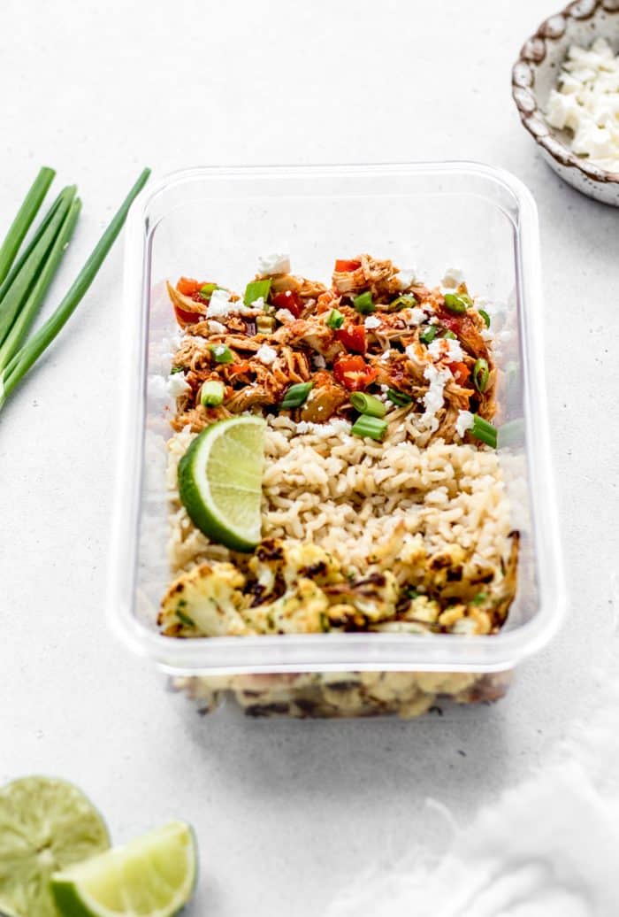 Buffalo chicken, rice and cauliflower in a box with a slce of lime and green onions.