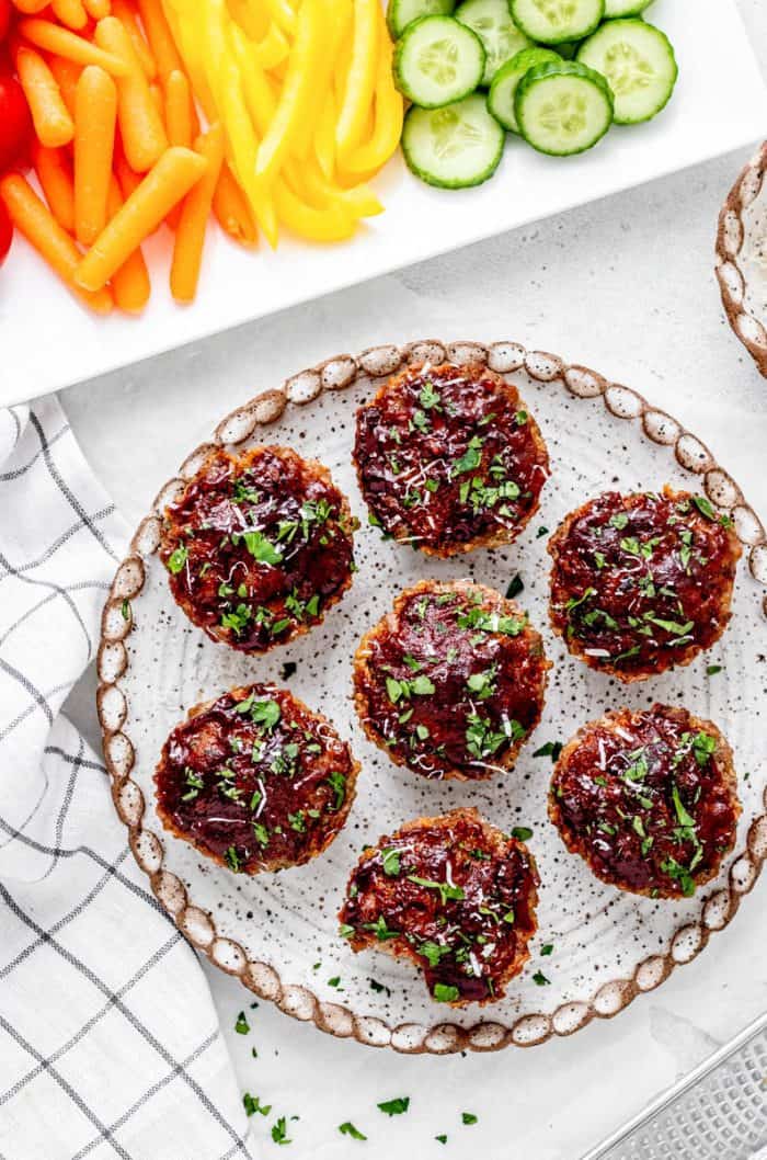 Overhead shot of beef and quinoa baby meatloaf muffins on a plate next to vegetables.