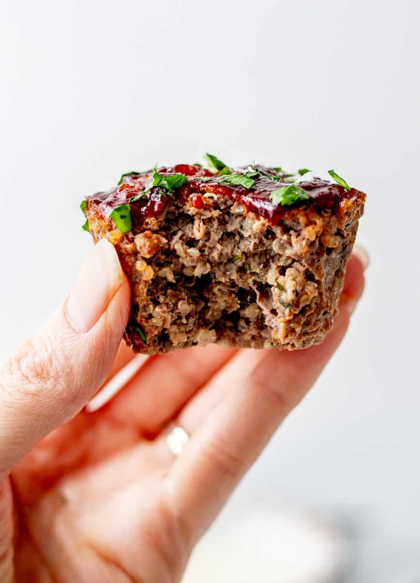 A hand holding up a beef and quinoa meatloaf muffin topped with BBQ sauce.