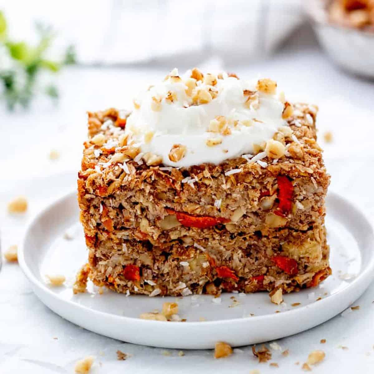 Two carrot cake oatmeal bars on a plate stacked on top of each other.