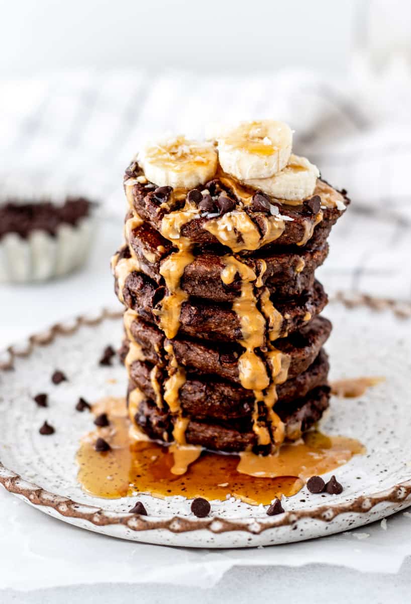 A tall stack of chocolate protein pancakes on a plate with toppings.